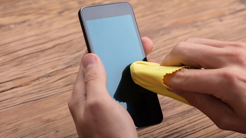 Un smartphone est en train d'être nettoyé avec une chiffonette pour écran.